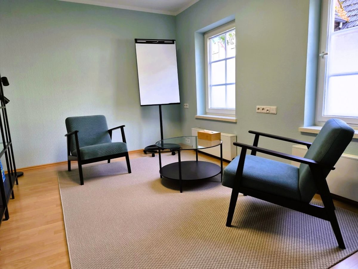 Einblick in den Praxisraum für Einzeltherapie in Kirchheim unter Teck mit gemütlichen Sesseln, Fachbibliothek und Flipchart.